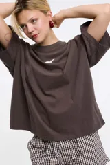 Remera de corte boxy color gris oscuro, con cuello redondo y mangas cortas. Presenta un diseño estampado localizado en la parte superior del pecho.