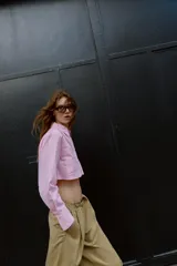 Camisa corta rosa con rayas verticales finas, cuello solapa, manga larga y bolsillos delanteros de plastrón. Cierre frontal con botones ocultos.