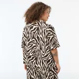 Blusa de punto crepé con estampado animal print tipo cebra en tonos marrón y crema. Presenta cuello solapa, cierre frontal con botones y mangas cortas de corte holgado.