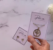 Conjunto de accesorios compuesto por un collar con dije circular que contiene una libélula en su interior y un par de aros tipo stud con forma de libélula, confeccionados en acero quirúrgico.
