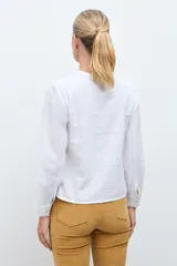 Blusa blanca de manga larga con cuello redondo, confeccionada en tela liviana con detalles de encaje vertical y bordado floral en el pecho.