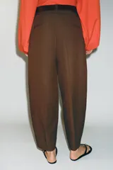 Pantalón tiro bajo color marrón, de corte globo y pernera recta con raya marcada al frente. Incluye trabillas y un cinturón marrón oscuro con hebilla metálica.