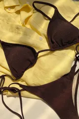 Conjunto de bikini marrón con lurex, compuesto por un corpiño triangular con breteles regulables y espalda para atar, con copas desmontables, y una bombacha semivedetina con tiras laterales para atar.