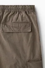 Pantalón cargo de sarga de algodón suave con efecto lavado, color marrón verdoso. Presenta cintura elástica con cordón ajustable, bolsillos laterales, bolsillos cargo con solapa en las piernas y cordón ajustable en el bajo. Corte holgado.