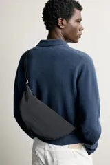 Bolso de hombro de nylon color negro, con diseño curvo y cierre de cremallera en el compartimento principal. Cuenta con asa ajustable para llevar al hombro y bolsillo interior con cierre.