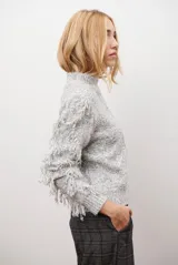 Buzo de punto color beige con cuello redondo, mangas largas con flecos decorativos y diseño de trenzas en el frente.