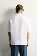 Camisa regular fit confeccionada en tejido de lino, color blanco, con cuello solapa, manga corta y cierre frontal de botonadura.