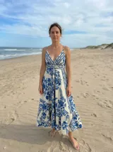 Vestido largo de verano, color blanco con estampado floral en azul índigo. Presenta tirantes finos, escote en V cruzado y un cinturón fino del mismo tejido que marca la cintura. La falda es amplia con volados.