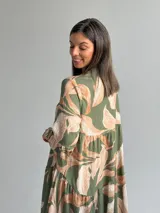 Vestido largo verde con estampado botánico en tonos tostados, escote en V con botones frontales, mangas largas abullonadas y diseño en niveles con volados.