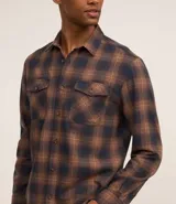 Camisa de manga larga confeccionada en franela de algodón, con diseño de cuadros en tonos marrones y azul marino. Presenta cuello inglés, cierre frontal con botones y dos bolsillos con solapa en el pecho.
