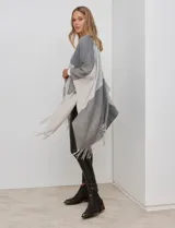 Ruana tejida con diseño colorblock en tonos de gris y beige, con flecos en el borde inferior.