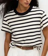 Remera de corte boxy confeccionada en algodón, con diseño de rayas horizontales en blanco y negro, cuello redondo en color negro contrastante y mangas cortas.