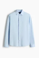 Camisa de manga larga en tejido elástico de mezcla de algodón, con cuello italiano, cierre frontal de botones y puños ajustables. Presenta un corte entallado slim fit y bajo redondeado.