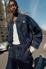 Chaqueta estilo bomber de Zara confeccionada en tejido denim azul oscuro. Presenta cuello solapa, cierre frontal con cremallera, bolsillos delanteros con solapa y bajo elástico que le otorga un ajuste ceñido en la cintura.