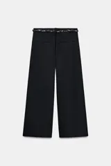 Pantalón de popelina de tiro alto y pernera ancha, de color negro. Presenta pinzas delanteras, bolsillos laterales y falsos bolsillos de vivo en la espalda. Incluye un cinturón combinado tipo pañuelo trenzado con tiras colgantes y cuentas de madera. Cierre frontal con cremallera, botón interior y gancho.