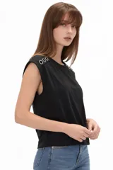 Remera de algodón blanca, de corte holgado y sin mangas, con cuello a la base y detalle de ojalillos metálicos sobre los hombros.
