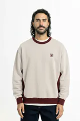 Buzo beige de corte oversize con cuello redondo y ribete burdeos en cuello, puños y cintura. Presenta paneles laterales burdeos con vivo blanco y logo Vernal bordado en el pecho.