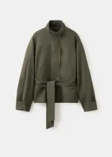 Chaqueta de lino color verde militar, diseño oversize con cuello alto, cierre oculto, manga larga con puño abotonado y cinturón ajustable en la cintura.