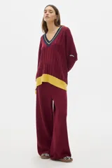 Buzo tejido de punto con diseño oversized, cuello en V y mangas largas. Presenta un patrón de trenzas verticales y detalles en contraste de color amarillo en el ruedo y los puños, además de un borde azul marino en el cuello.