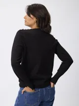 Buzo de punto fino color marrón topo, con cuello redondo y detalle de botones decorativos dorados sobre el hombro izquierdo. Presenta mangas largas con puños acanalados y una pequeña abertura lateral en los mismos.