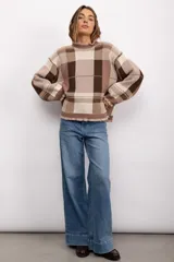 Sweater de punto con diseño de cuadros escoceses en tonos marrones y beige. Presenta un corte oversize, cuello redondo y terminaciones con volados en el cuello y los puños.