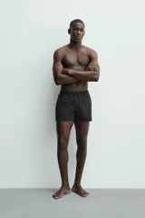 Short de baño negro de tejido técnico con estructura ripstop resistente a desgarros, cintura ajustable con cordón y bolsillos laterales.