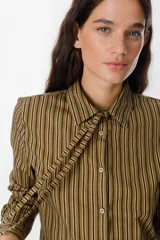 Camisa de manga larga con estampado de rayas verticales en tonos marrón, negro y blanco. Presenta cuello clásico, cierre frontal con botones y lazos decorativos en el cuello.