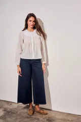Blusa blanca de algodón peinado con mangas largas, cuello babero bordado y pliegues frontales.