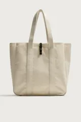 Bolso tipo shopper de tejido color crudo, con doble asa de hombro y detalles en cuero negro. Cuenta con compartimento principal con cierre de tira y botón a presión.