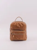 Mochila de cuero natural color suela, con diseño clásico y refinado. Cuenta con un compartimento principal con cierre, un bolsillo frontal con cierre y un asa superior. El diseño incluye detalles de costuras y herrajes metálicos.