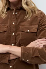 Camisa de pana color tostado, con cuello clásico, cierre frontal con botones metálicos y bolsillos frontales con solapa.