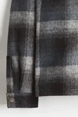 Sobrecamisa de corte relajado en tejido suave con diseño a cuadros. Presenta cuello inglés, cierre frontal con botones a presión, hombros caídos y mangas largas con puños abotonados.