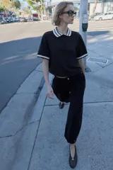 Top de tejido negro con cuello polo y bordes de manga cortos con diseño de ondas en blanco y negro. Tiene un cierre frontal de botones.