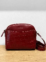 Bandolera semirrígida Sagali de cuero vacuno color bordó, con textura de cocodrilo en el bolsillo frontal y cuerpo liso. Cuenta con cierre superior y correa regulable.