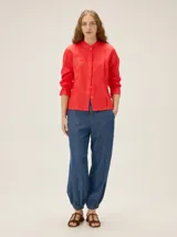 Camisa de lino color rojo de silueta relajada, con cuello mao, alforzas verticales, mangas largas con volumen y puños elastizados, y detalle de bordado en el pecho.
