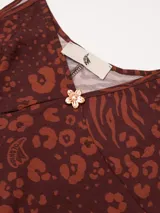 Vestido largo de corte fluido con escote en V profundo y finos breteles. Presenta un estampado animal print combinado con rayas y un detalle decorativo de flor en cobre en el centro del escote.