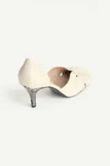 Zapato de tacón de piel color beige, con detalle cruzado en la parte delantera y tacón alto fino combinado con acabado en punta redonda.