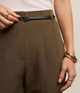 Pantalón de sastrería corte carrot, color beige, con cintura alta, pinzas frontales y cinturón fino incorporado con hebilla metálica.