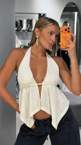 Top halter de tejido de punto color blanco, con escote en V pronunciado, diseño abierto en el frente y bajo asimétrico en punta.