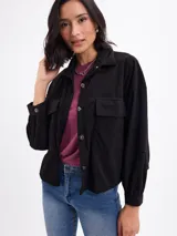 Campera de pana negra con cierre frontal de botones metálicos, cuello clásico y dos bolsillos frontales con solapa. Presenta mangas largas con puños abotonados y un diseño liviano sin forro.