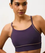 Top deportivo de microfibra en color violeta con detalles de friso en tono arena. Presenta un diseño de escote redondo, breteles finos y una banda inferior elástica que proporciona mayor sujeción. Incluye copas removibles para mayor comodidad.