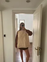 Buzo beige con mangas marrones y cuello lila, de corte holgado y largo a la cadera.