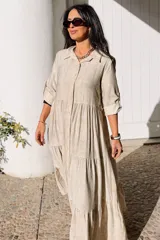 Vestido largo de estilo camisero en color azul, con cuello clásico, cierre frontal de botones y mangas tres cuartos con trabillas. Presenta un diseño de falda con cortes horizontales que le otorgan volumen y movimiento.