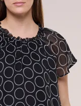 Blusa holgada de gasa negra con estampado geométrico de círculos blancos, cuello redondo fruncido con volados y mangas cortas de corte mariposa.