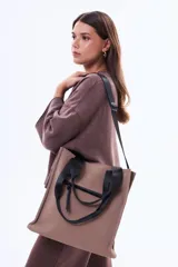 Bolso tipo tote color marrón, con diseño minimalista y moderno. Cuenta con asas de mano negras, correa ajustable para el hombro y un bolsillo frontal con cierre.