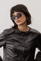 Chaqueta de cuero negra con cuello redondo, cierre frontal de botones forrados y bolsillos ribeteados con detalles de costura decorativa.