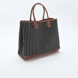 Bolso tipo tote de tela a rayas verticales blancas y negras, con detalles de cuero sintético color suela en la base, manijas y bordes.