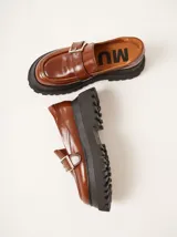 Mocasines de cuero color marrón con plataforma dentada negra. Presentan una tira frontal con hebilla metálica dorada y costuras decorativas en contraste.