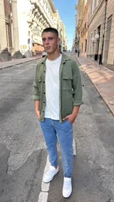 Sobrecamisa de color verde militar, confeccionada en tejido resistente, con cuello clásico, cierre frontal de botones y dos bolsillos frontales con solapa en el pecho.