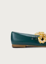 Bailarina de cuero color verde oscuro con detalles de ojales metálicos plateados y lazo desmontable de tela a cuadros amarillos y blancos. Presenta una silueta clásica con punta redondeada y suela plana.